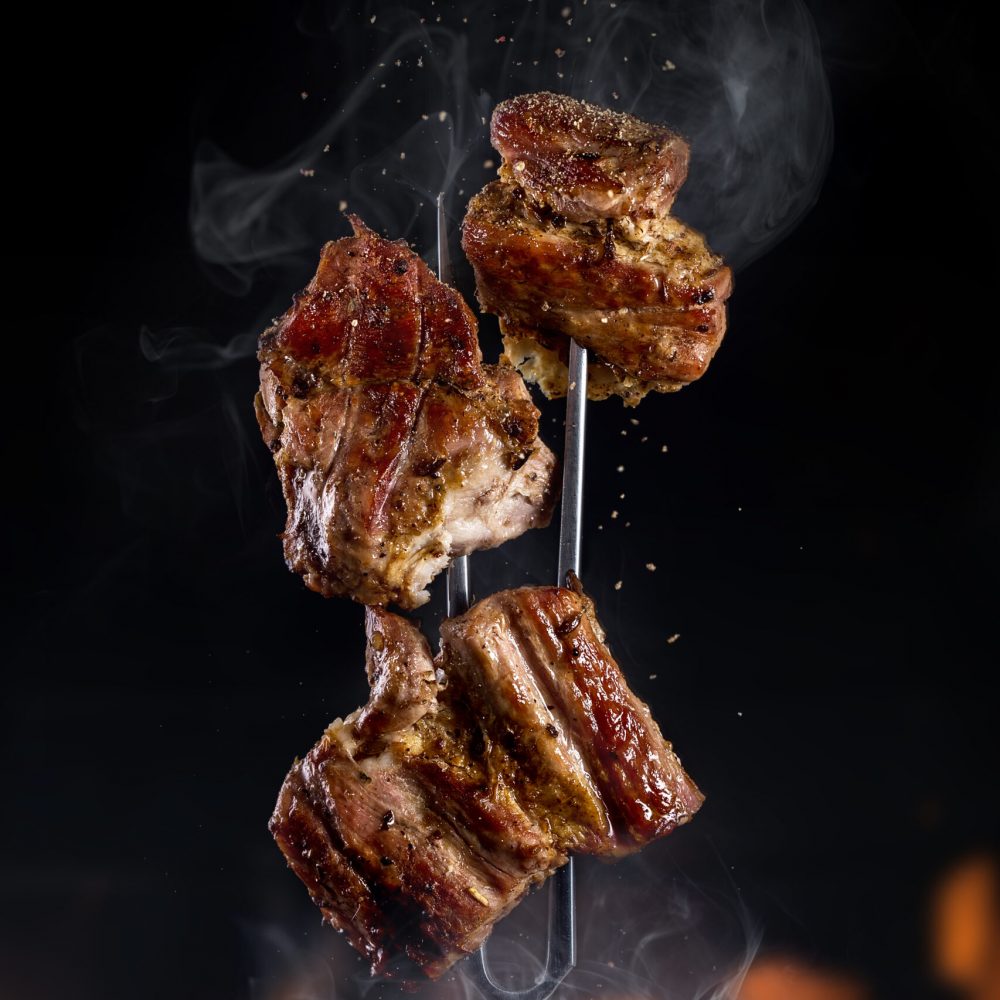 Fork with pieces of delicious barbecued meat on black background Fork with pieces of delicious barbecued meat on black background, with fire flames. Tasty meat. Space for text
